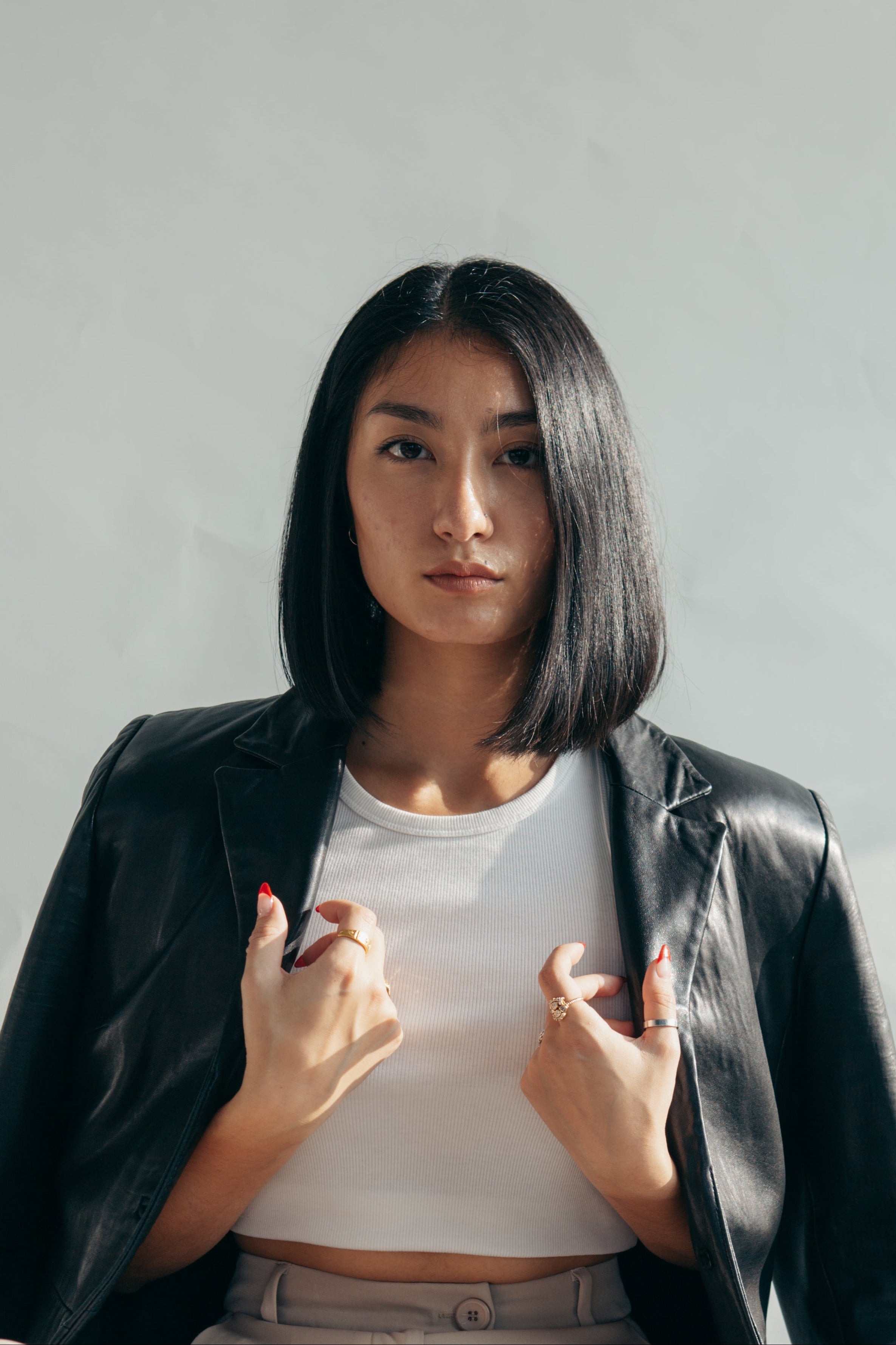 Woman wearing a black leather jacket over a white shirt against a plain background